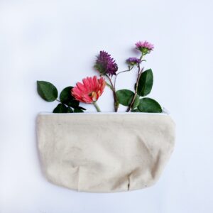 Pink and purple wildflowers with their leaves popping up out of a small zippered canvas bag.