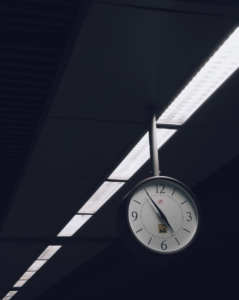 analog clock at 5:55 pm hanging from a fluorescent light normally found in corporate workspaces